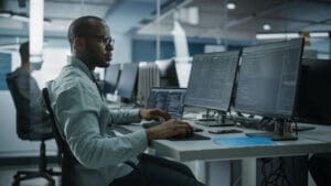 African American man typing at computer on table in front of multiple monitors
